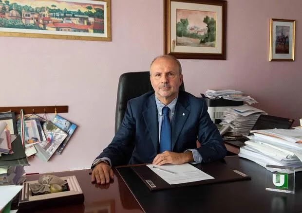 Orazio Schillaci seated at a large wooden desk covered with papers in an office decorated with framed paintings