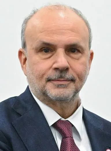 Portrait of Orazio Schillaci against a white background, wearing a dark suit, white shirt and burgundy tie