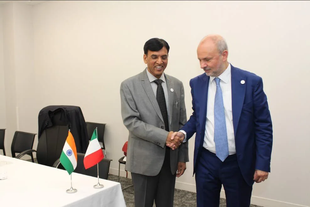 Orazio Schillaci shaking hands with an Indian official in a meeting room, with small Indian and Italian flags on the table