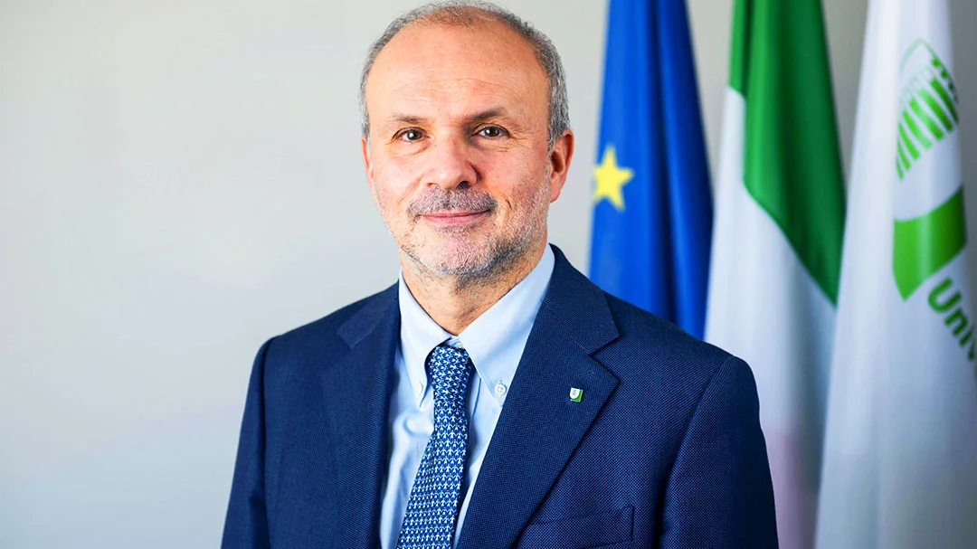 Orazio Schillaci smiling in a navy suit in front of the European Union flag, the Italian flag and a green institutional banner