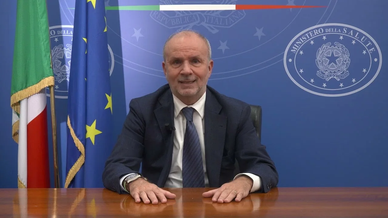 Orazio Schillaci seated at a desk in the Ministry of Health briefing room, with the Italian and European flags behind him