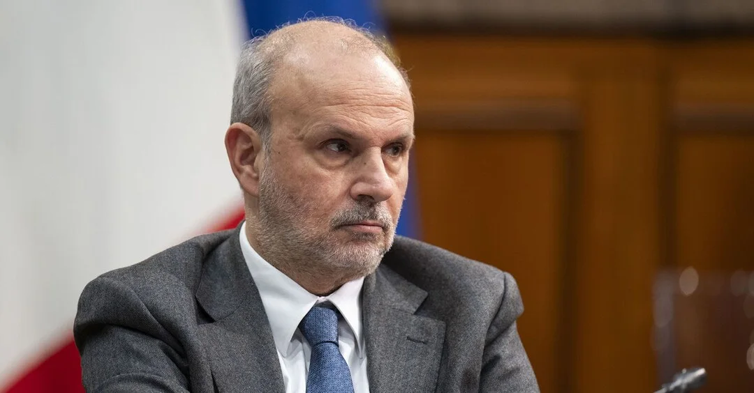 Orazio Schillaci in a grey suit listening attentively during an institutional session, with the Italian flag to his side