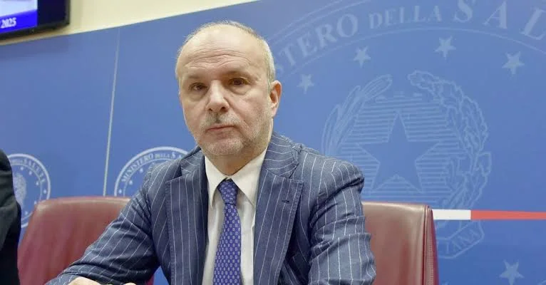 Orazio Schillaci in a pinstriped suit seated at a briefing in front of the emblem of the Ministry of Health